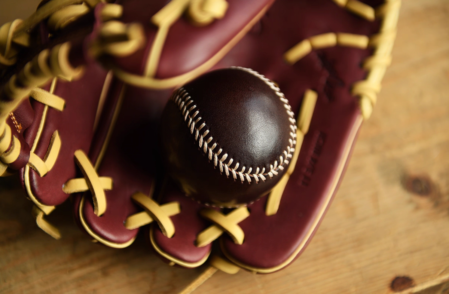 Dark brown full-grain leather baseball placed inside a burgundy baseball glove for display.