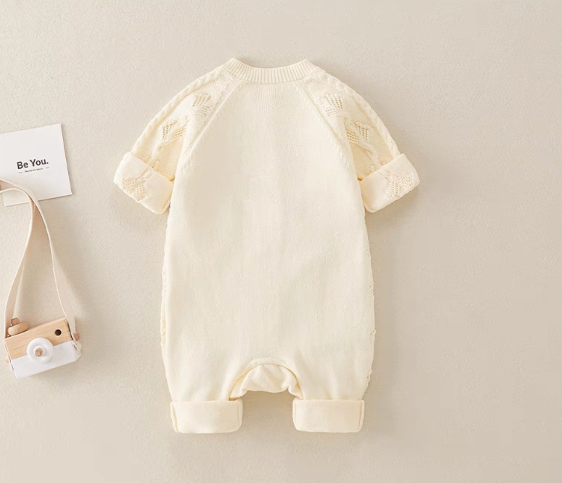 Back view of beige cable knit baby romper with smooth knit back and ribbed leg cuffs