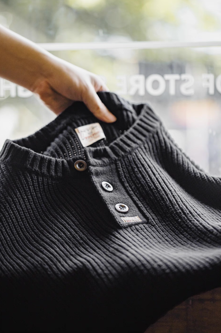 Hand holding black Henley sweater showing ribbed texture and collar.