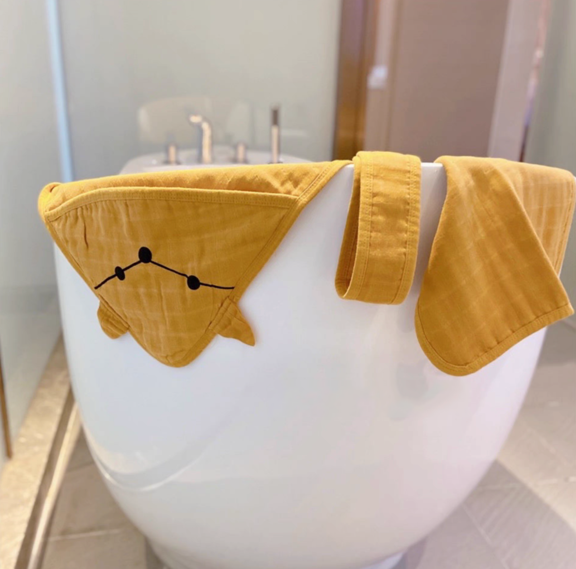 Fox Orange baby swaddle wrap with hood and matching belt draped over bathtub showing breathable cotton muslin texture