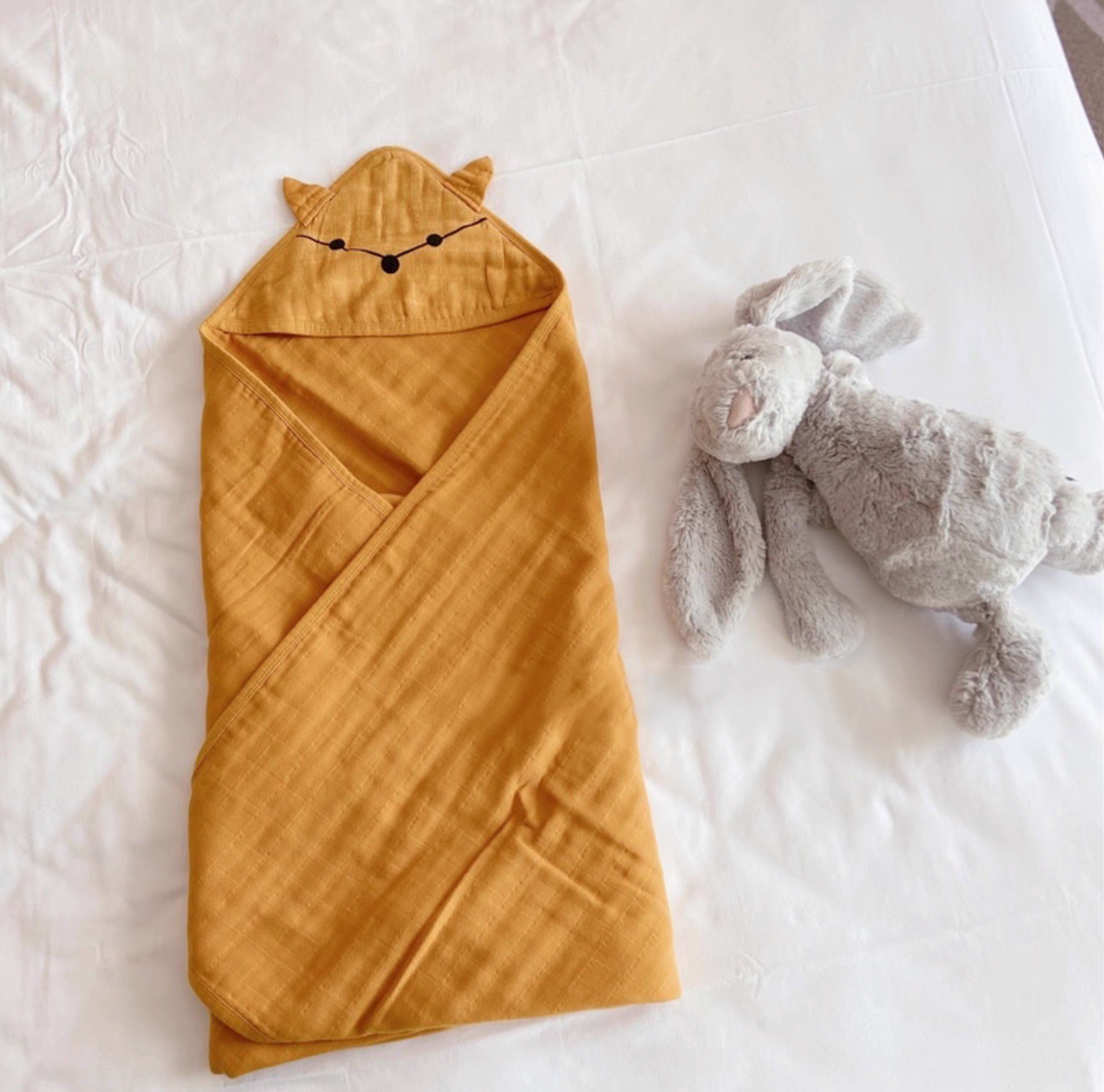 Fox Orange hooded baby swaddle wrap fully wrapped on bed with soft plush toy highlighting cozy cotton gauze fabric
