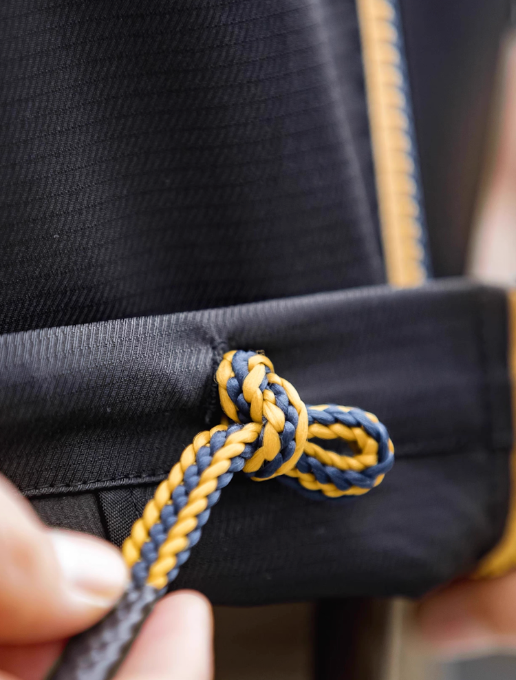 Close-up of black coach jacket yellow-blue braided drawstring hem.