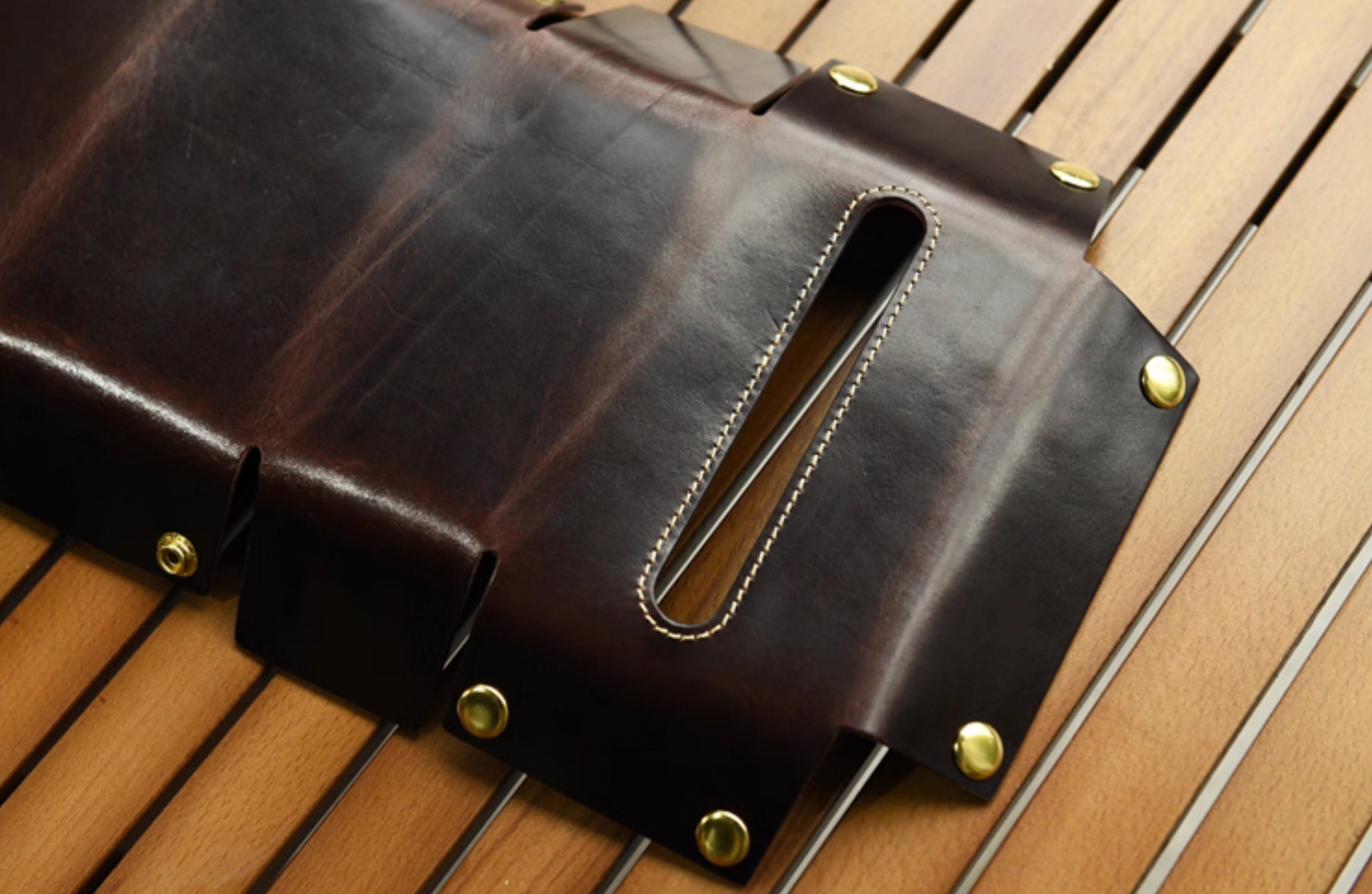 Unassembled dark brown leather tissue box laid flat showing cutouts and brass buttons.