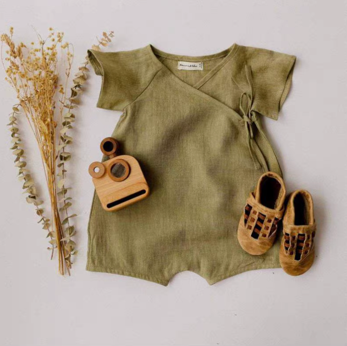 Green cotton muslin baby romper styled with small shoes and toy accessories