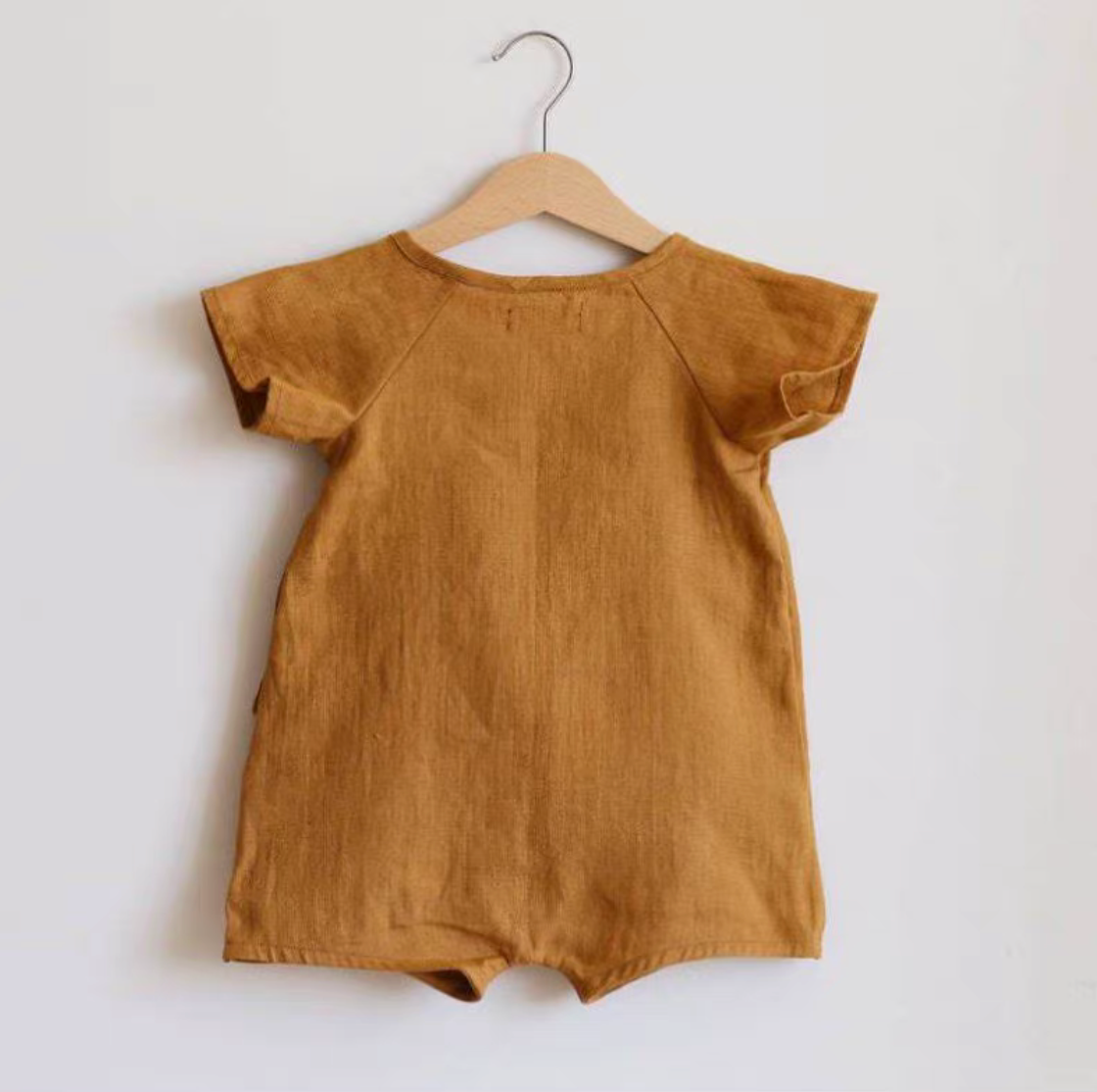 Back view of mustard lightweight cotton muslin baby romper on hanger