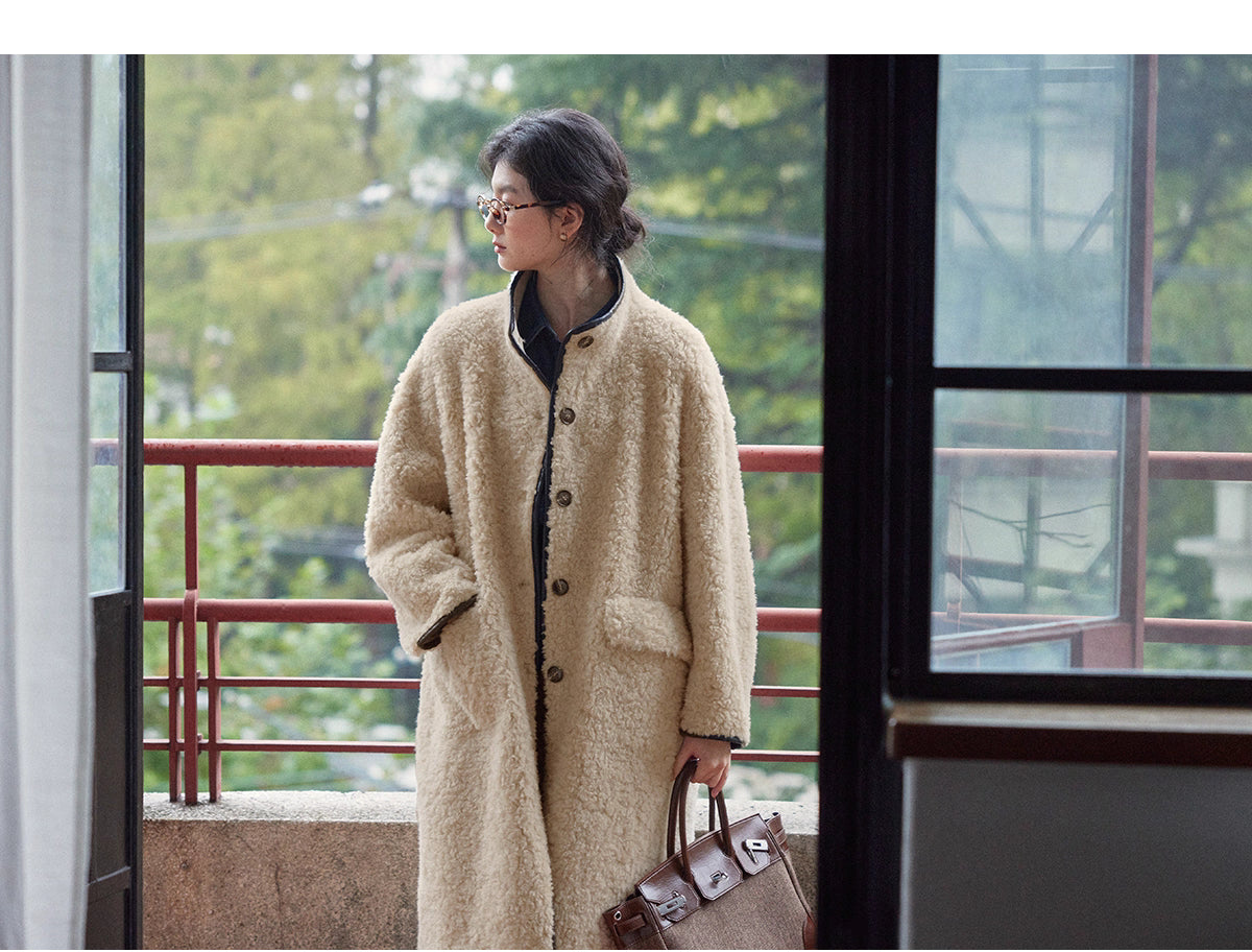 Full-length shot of woman wearing long beige wool shearling coat with brown leather bag.