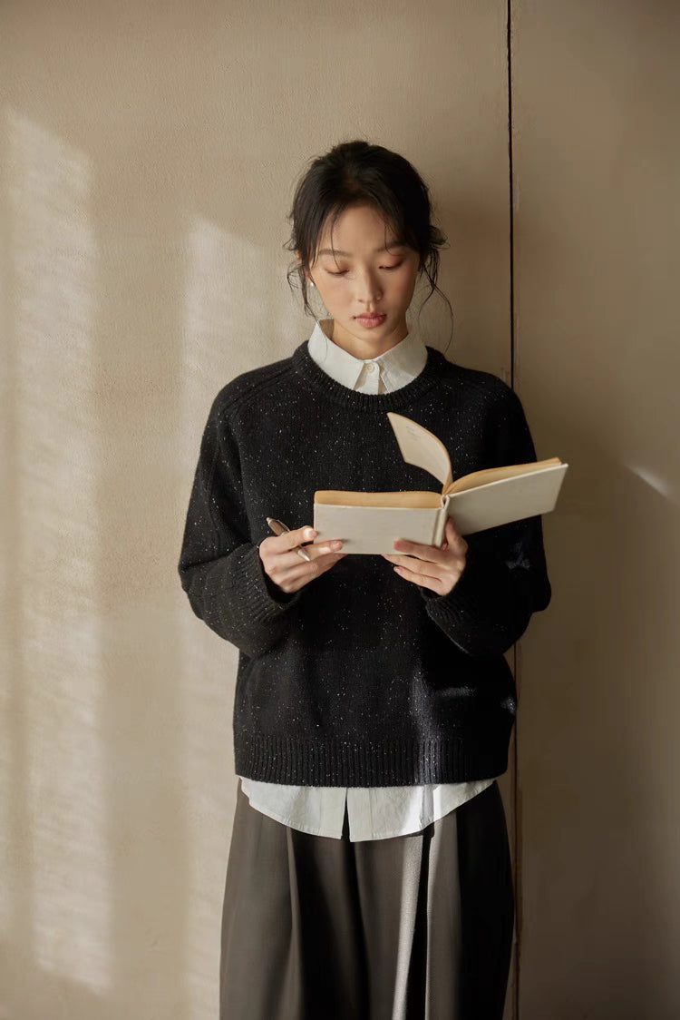 Black speckled merino wool sweater worn while reading in warm sunlight showcasing textured flecked knit