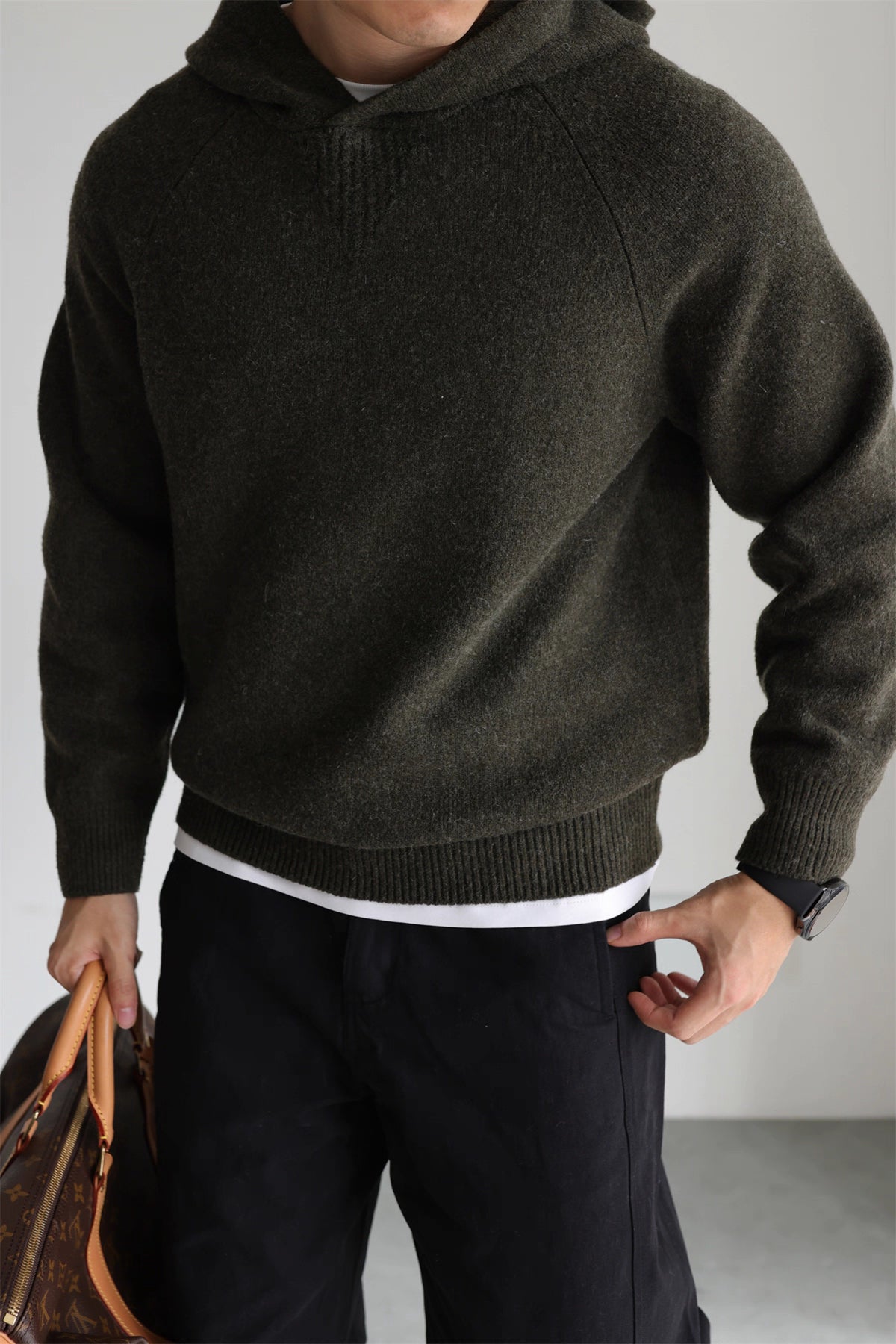 Olive knit hoodie styled with black pants and leather travel bag