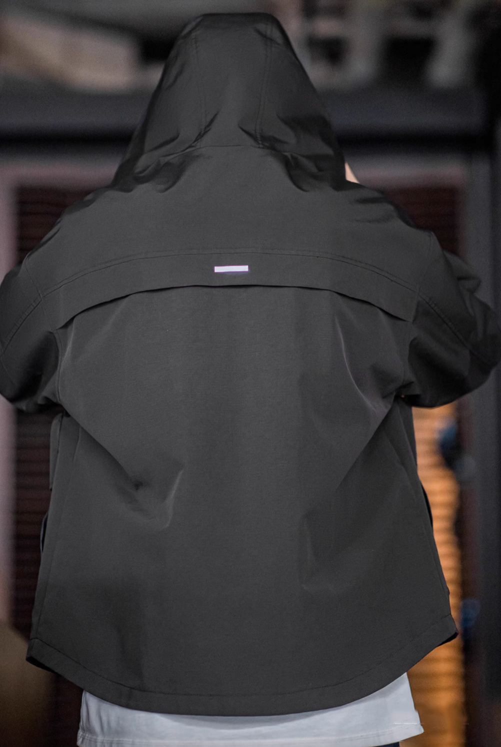 Back view of Black Metro Flex Waterproof Jacket showing hood shape, back rain guard panel and reflective strip detail