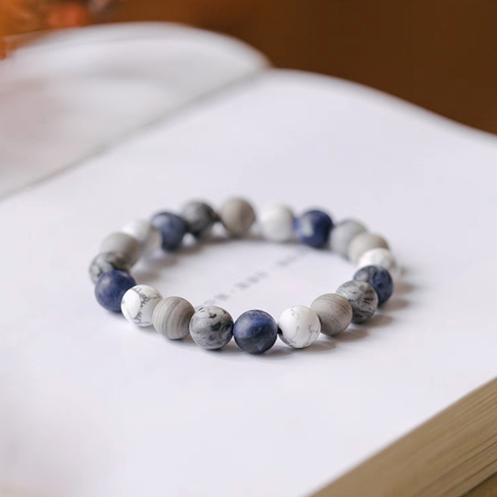 Mountain and sea gradient blue bracelet with white howlite, gray vein stone, and blue natural stone beads displayed on open book