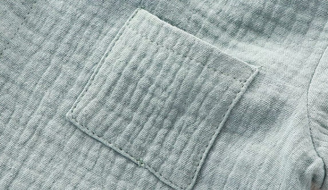 Close-up of light blue muslin baby romper chest pocket with textured cotton fabric
