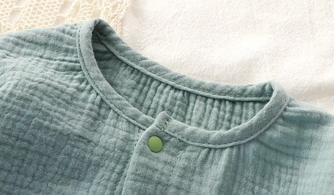 Close-up of light blue muslin baby romper neckline with snap button fastening detail