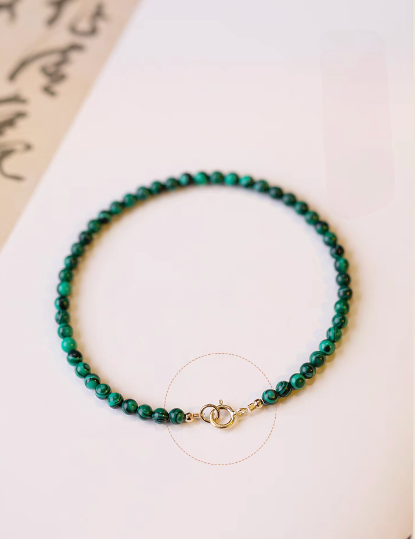 Top view of green malachite bracelet arranged in a full circle highlighting gold clasp closure and rich banded stone texture