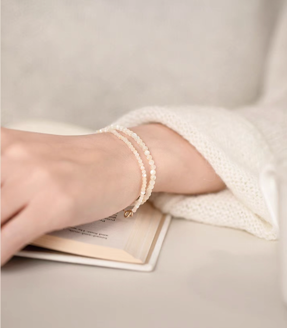 Natural white mother-of-pearl bracelets styled in a double-wrap look on a wrist beside an open book