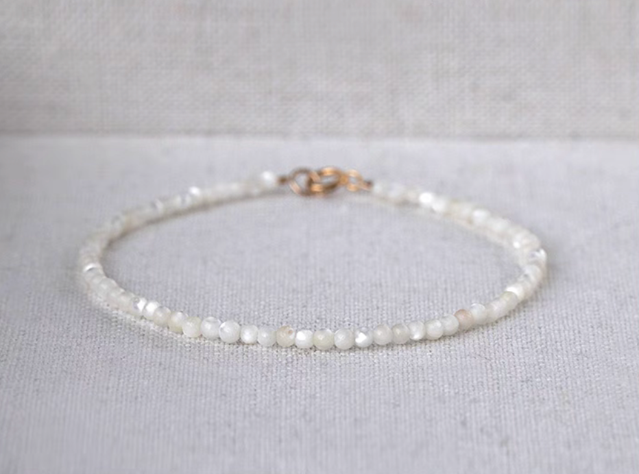 Natural white mother-of-pearl delicate bracelet displayed on fabric with a visible gold clasp and circular shape