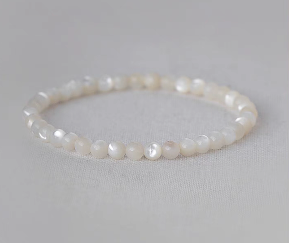 Natural white mother-of-pearl round bead bracelet displayed in a circular shape on pale fabric background