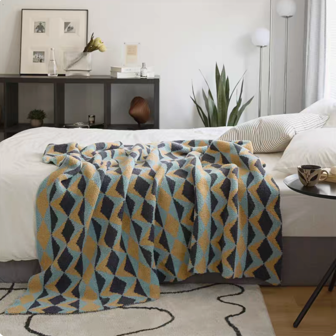 Alonso geometric chenille throw blanket with blue and mustard diamond pattern draped over bed