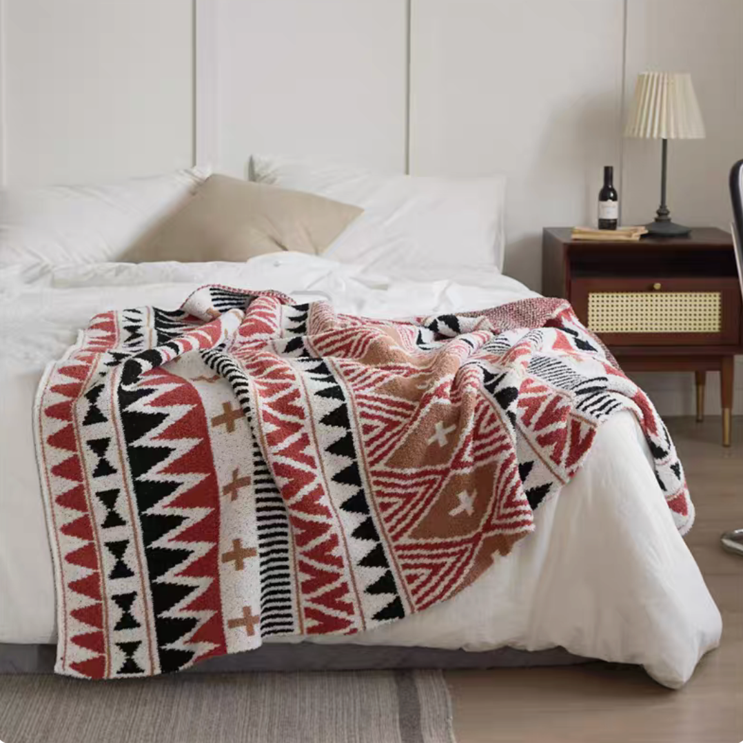 Hess chenille throw blanket with tribal geometric red and black pattern layered on bed