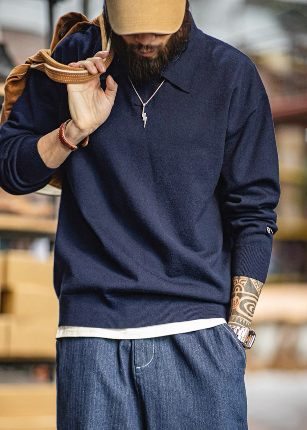 Model wearing navy blue knit polo sweater with khaki cap and casual jeans.