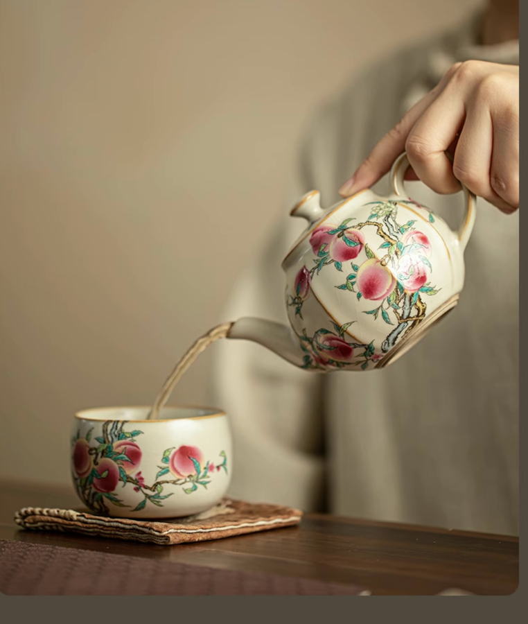 Nine Peach Ru Kiln Crackle Glazed Teapot in Nine Peach pouring tea into a matching teacup with peach design on a wooden table