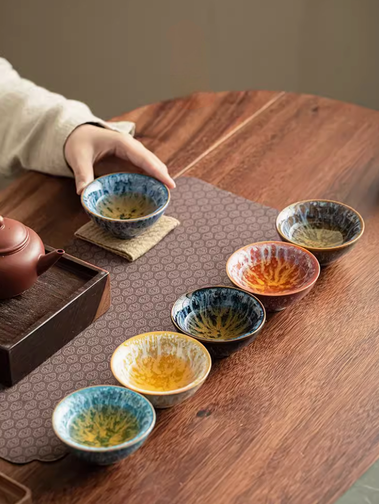 Nine-color kiln-glazed tea cups arranged on tea table during tea serving with teapot and traditional tea setting