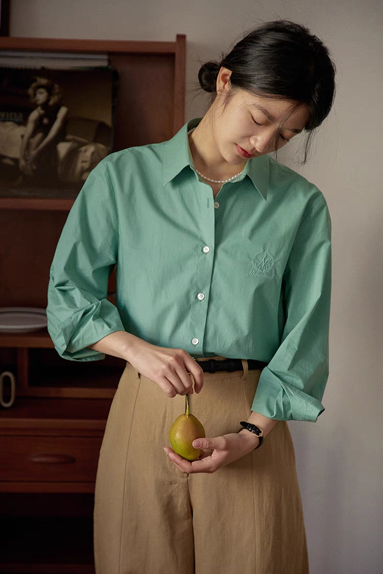 Green embroidered relaxed shirt worn while peeling fruit with soft indoor lighting emphasizing relaxed fit