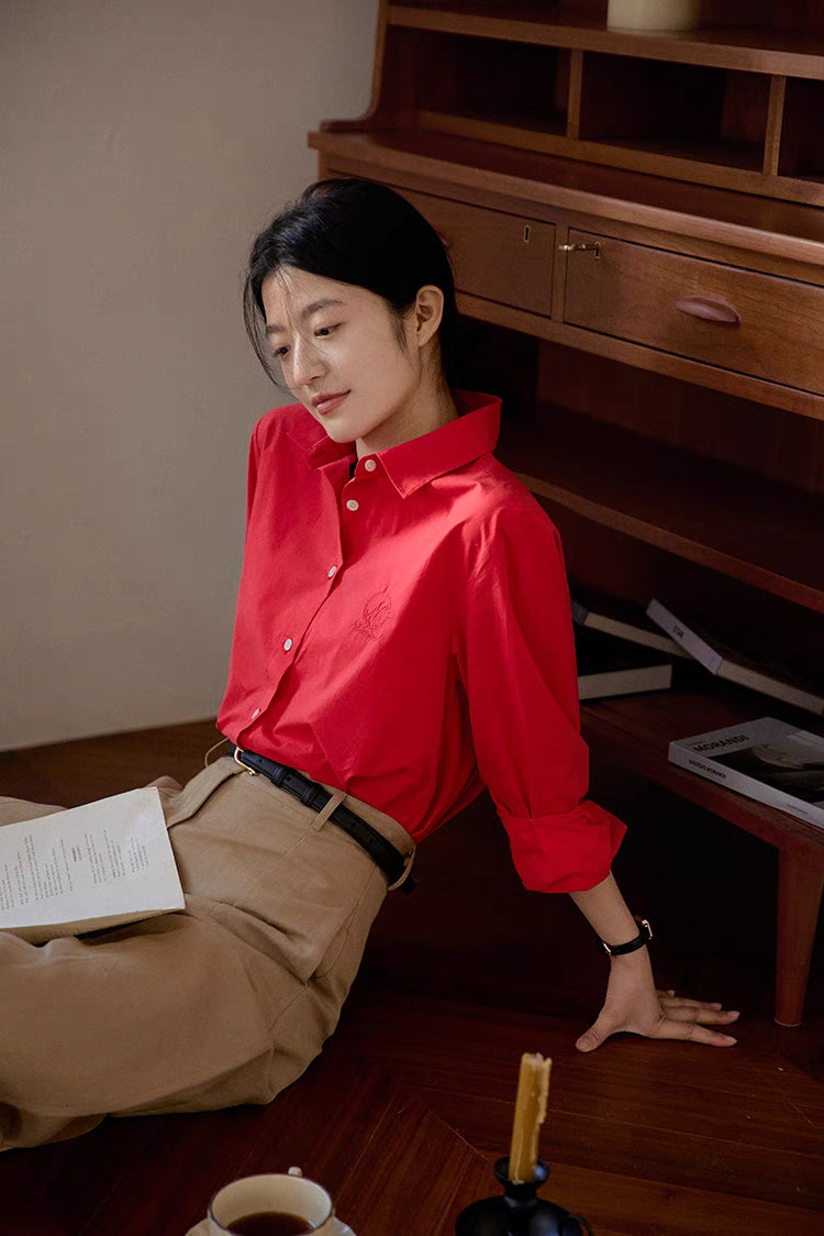 Red embroidered relaxed shirt styled while leaning on desk with soft lighting emphasizing relaxed silhouette and smooth texture