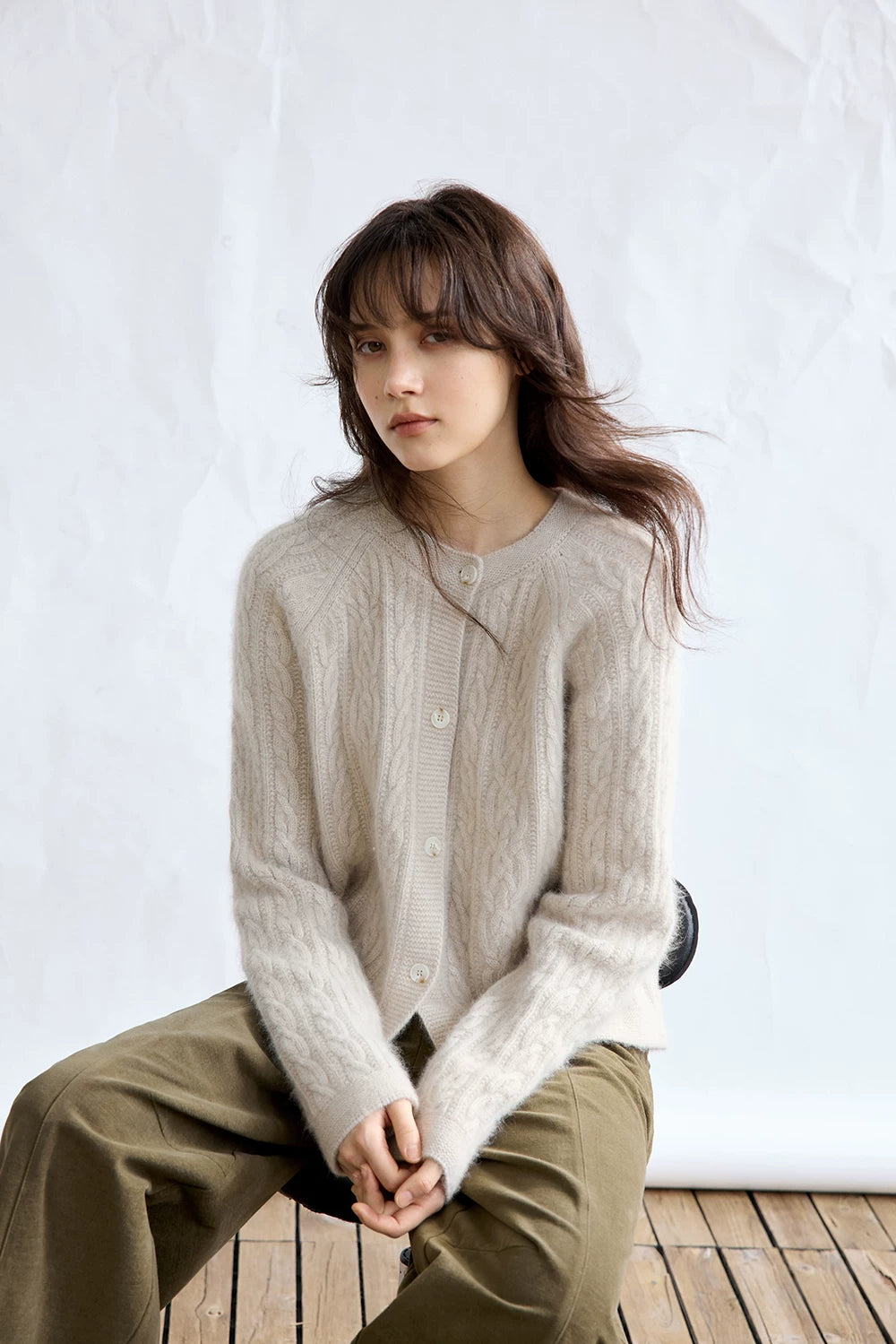Oatmeal cable-knit cardigan, seated front view showing button placket