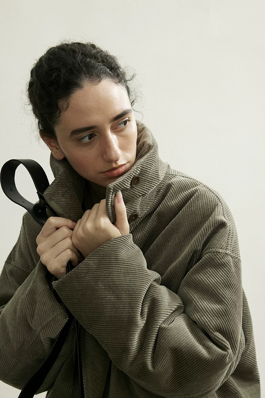 Close-up of an Olive Gray corduroy down jacket with the stand collar buttoned up to the chin