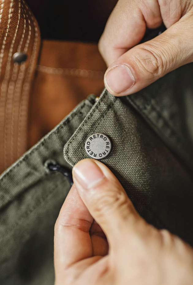 Close-up of olive green M-65 jacket button with retro branding detail