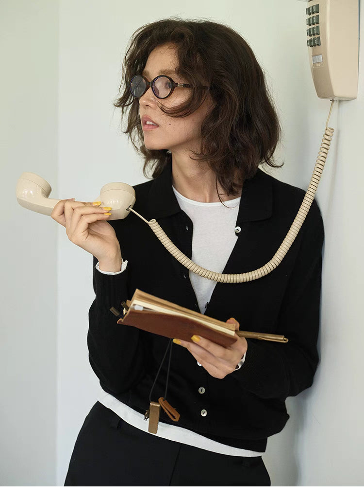 Model wearing black Poised Polo Knit Top with polo collar and button front, holding vintage telephone and notebook, front view