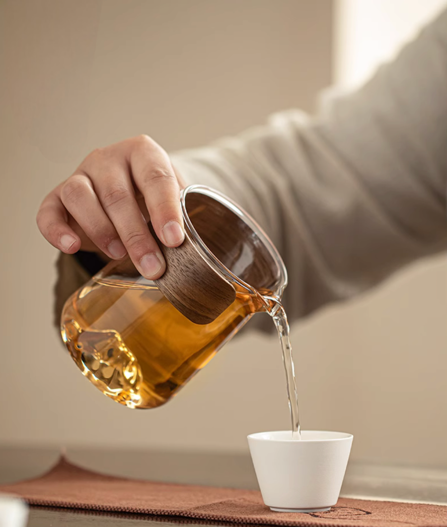 Glass teapot from white portable outdoor travel tea set pouring tea into ceramic cup