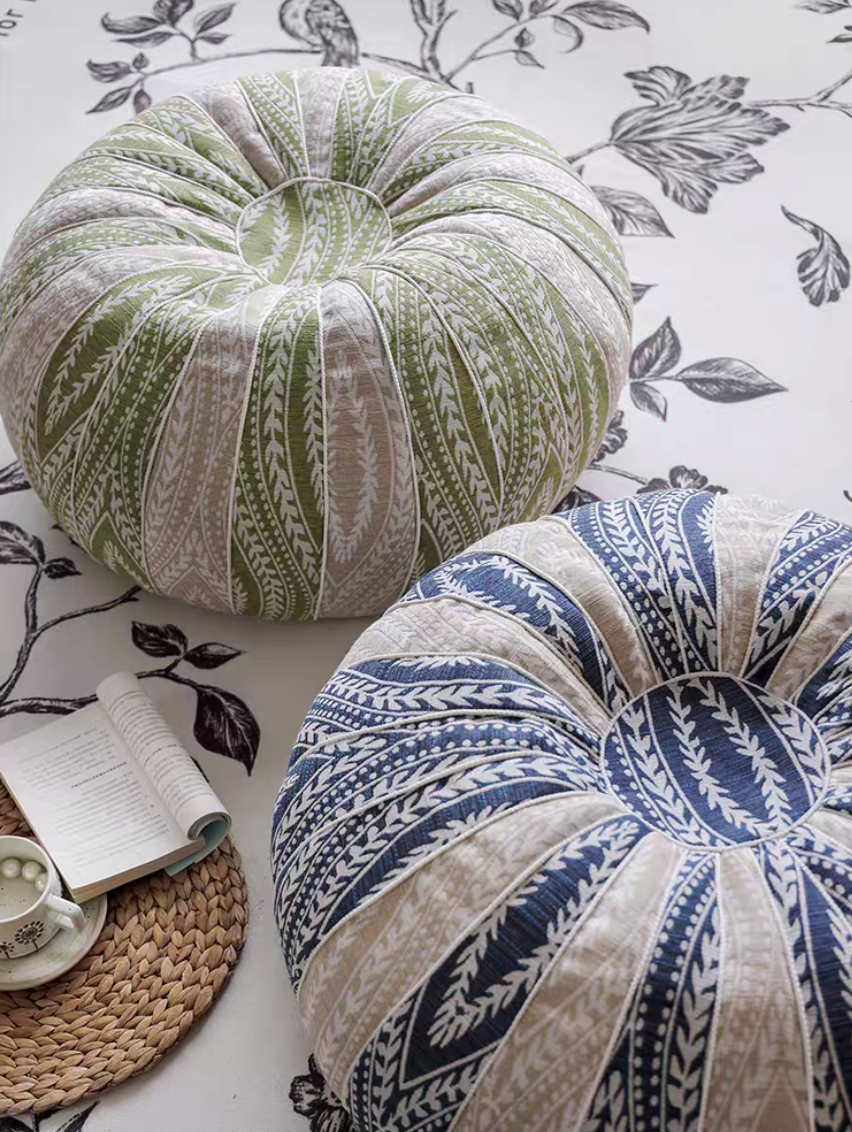 Top view of green and blue pumpkin round floor cushions on a patterned rug with a book and cup nearby