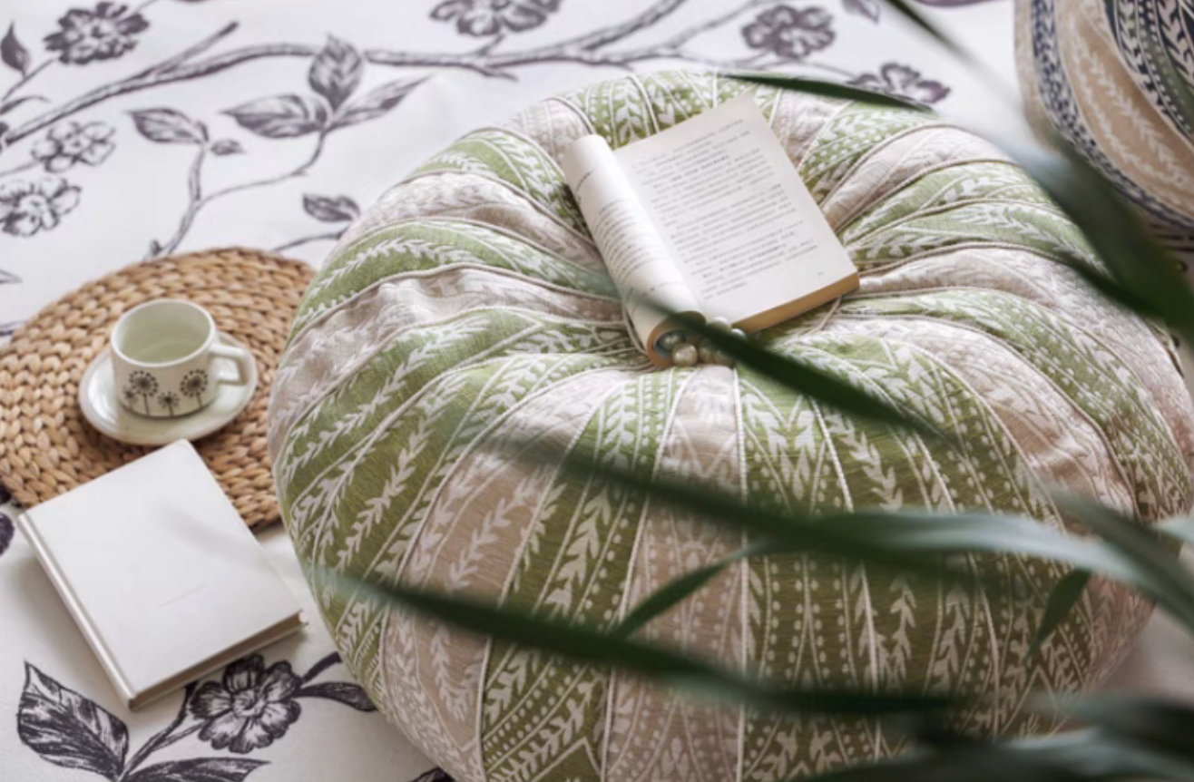 Close-up of green pumpkin round floor cushion with a book on top, styled for a cozy reading corner