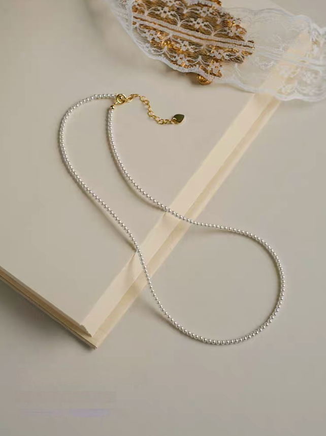Radiant Round Pearl Necklace in natural color displayed as a single strand on open book