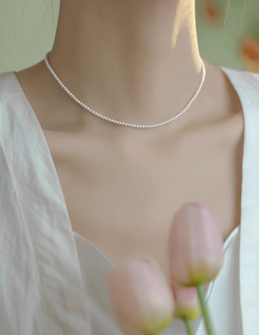Model wearing Radiant Round Pearl Necklace in natural color with pink tulips in foreground