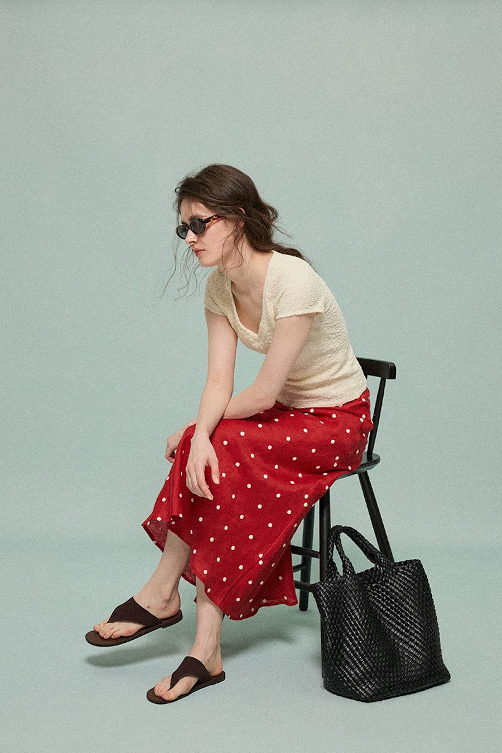 Model seated in a red embroidered polka dot midi skirt showing its fluid drape