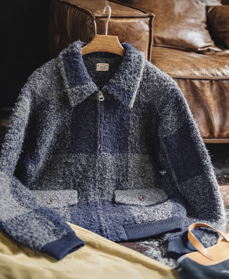 Blue-gray boucle plaid jacket hanging on wooden hanger beside leather sofa.