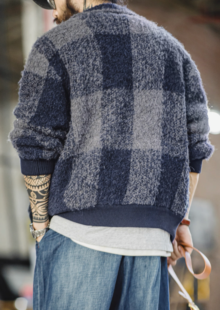 Model wearing blue-gray plaid boucle jacket viewed from behind outdoors.