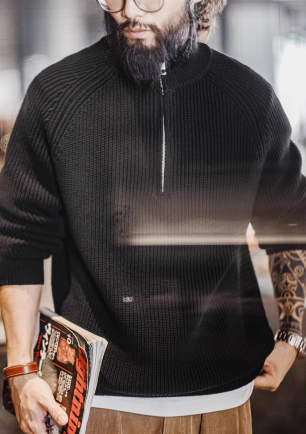Man wearing Ridge Half-Zip Pullover Sweater in Charcoal Black holding magazine highlighting ribbed knit fabric structured collar and casual modern styling