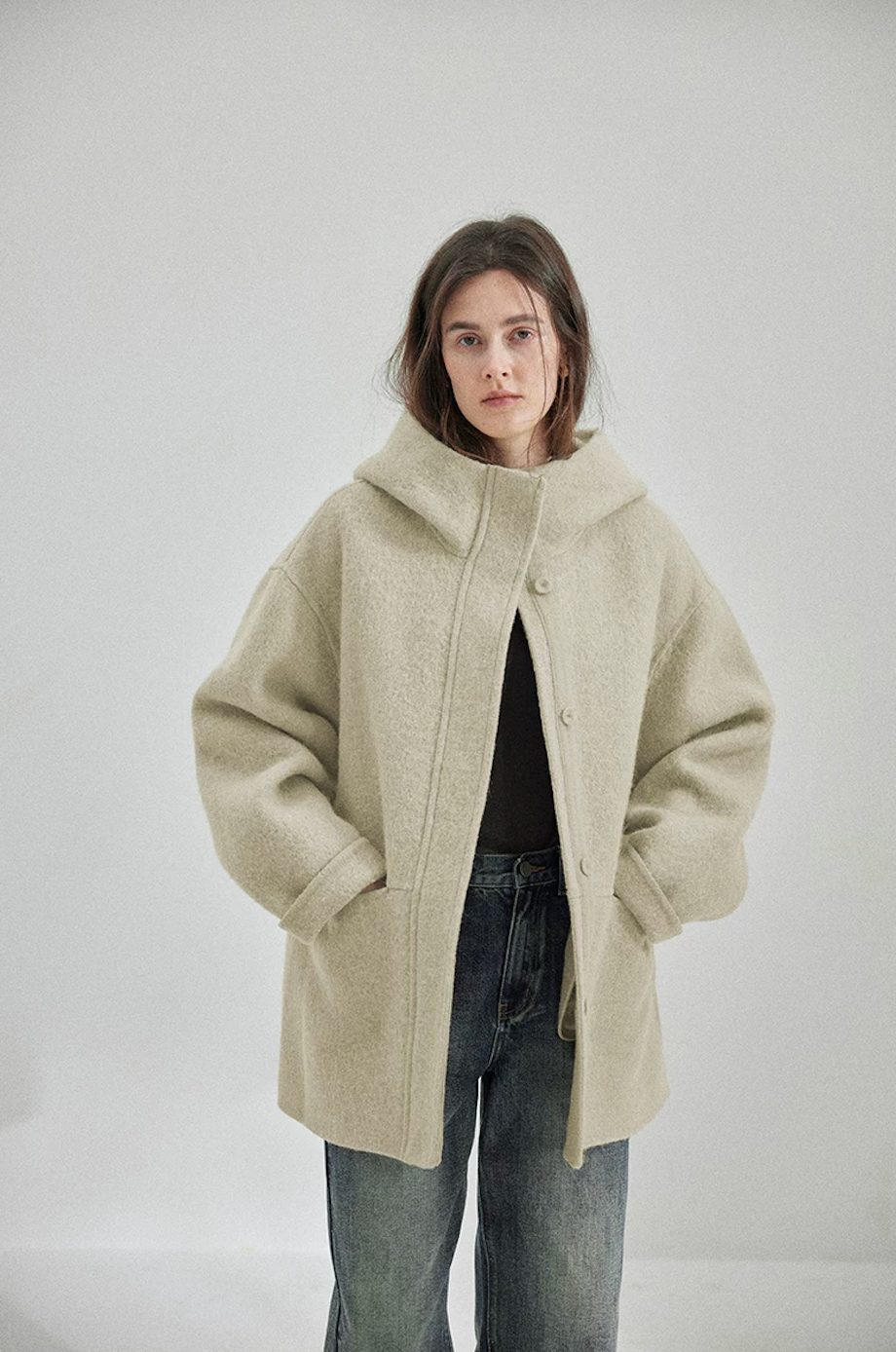 Sage oversized hooded wool coat worn partly open, showing self-fabric buttons and seam pockets