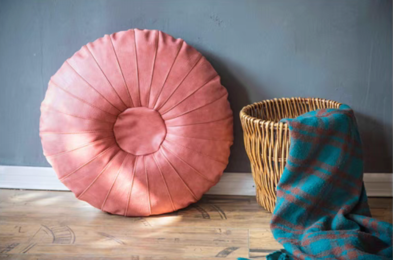 Pink Scandinavian round floor cushion standing upright beside basket with blanket in cozy setting