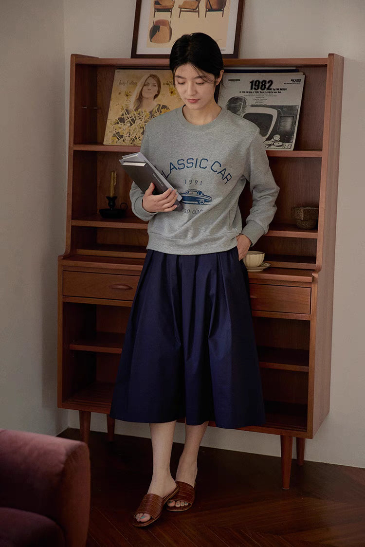 Casual outfit styling of The Sculptural Pleat A-Line Skirt in navy blue paired with sweatshirt highlighting versatile everyday wear and volume silhouette