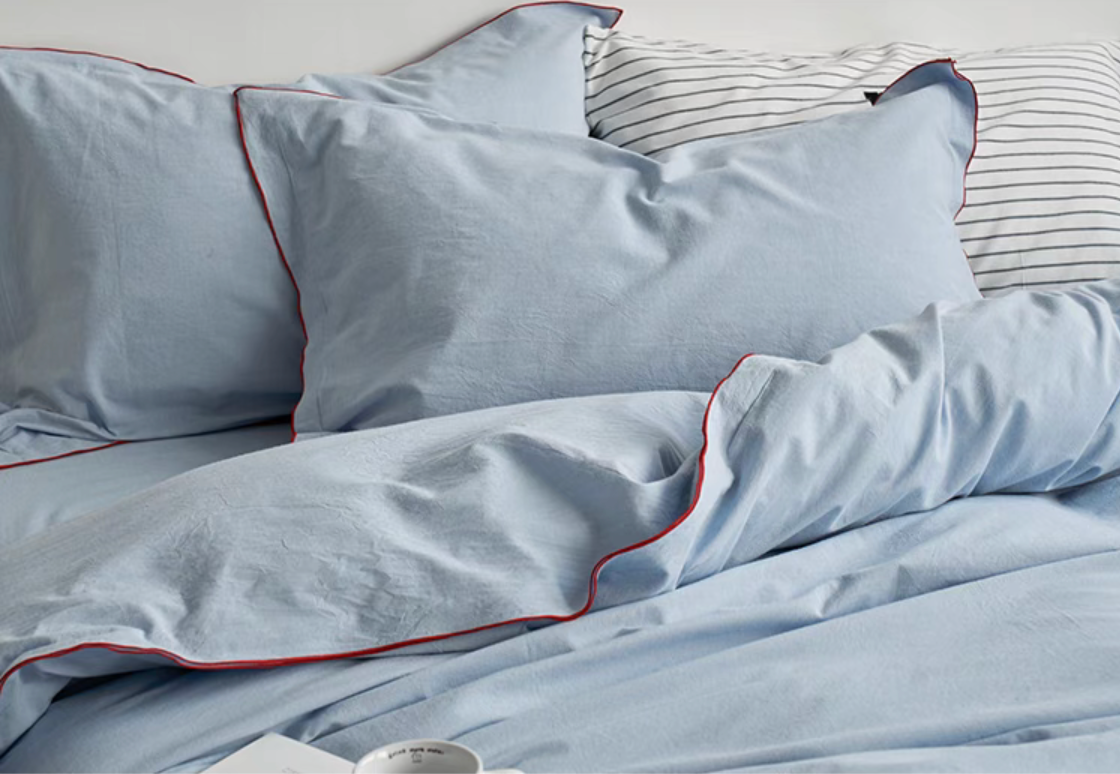 Light blue cotton duvet cover with red edge stitching draped across bed highlighting soft breathable cotton fabric