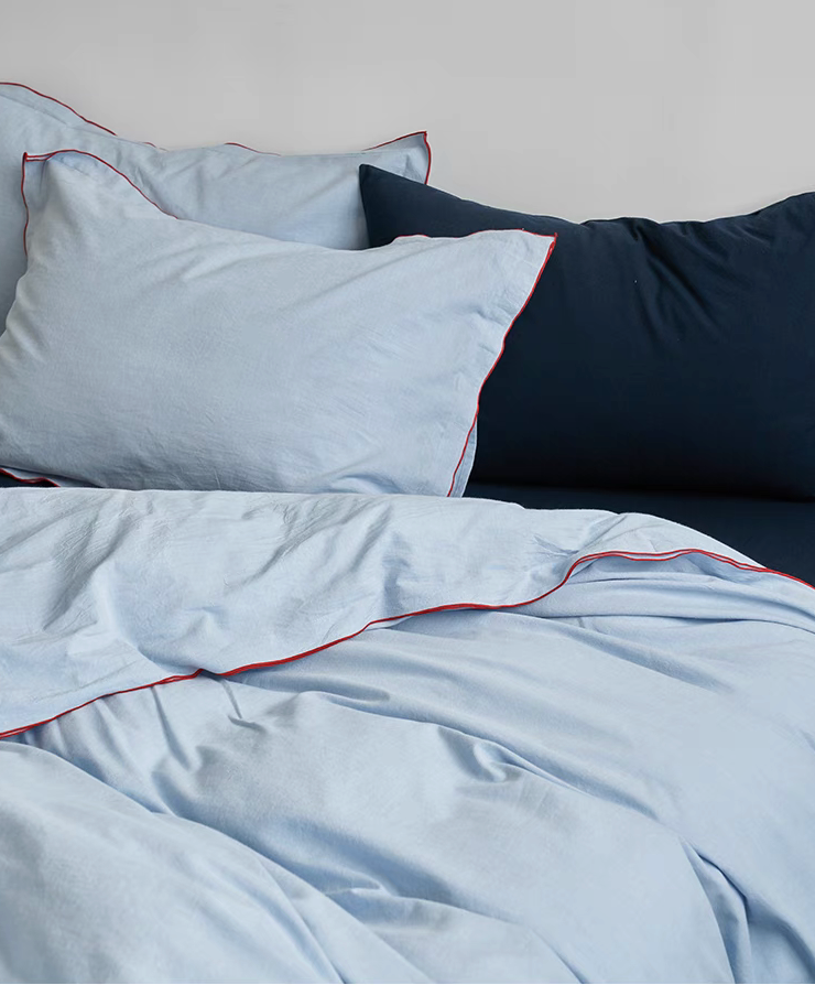 Skyline light blue cotton duvet set with red edge stitching layered over navy blue flat sheet creating modern contrast bedding look