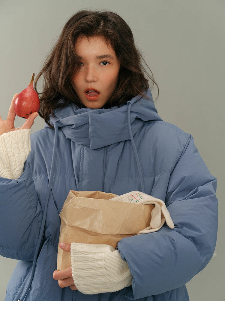 Close-up of dusty blue puffer jacket with the model holding a pear near her face.