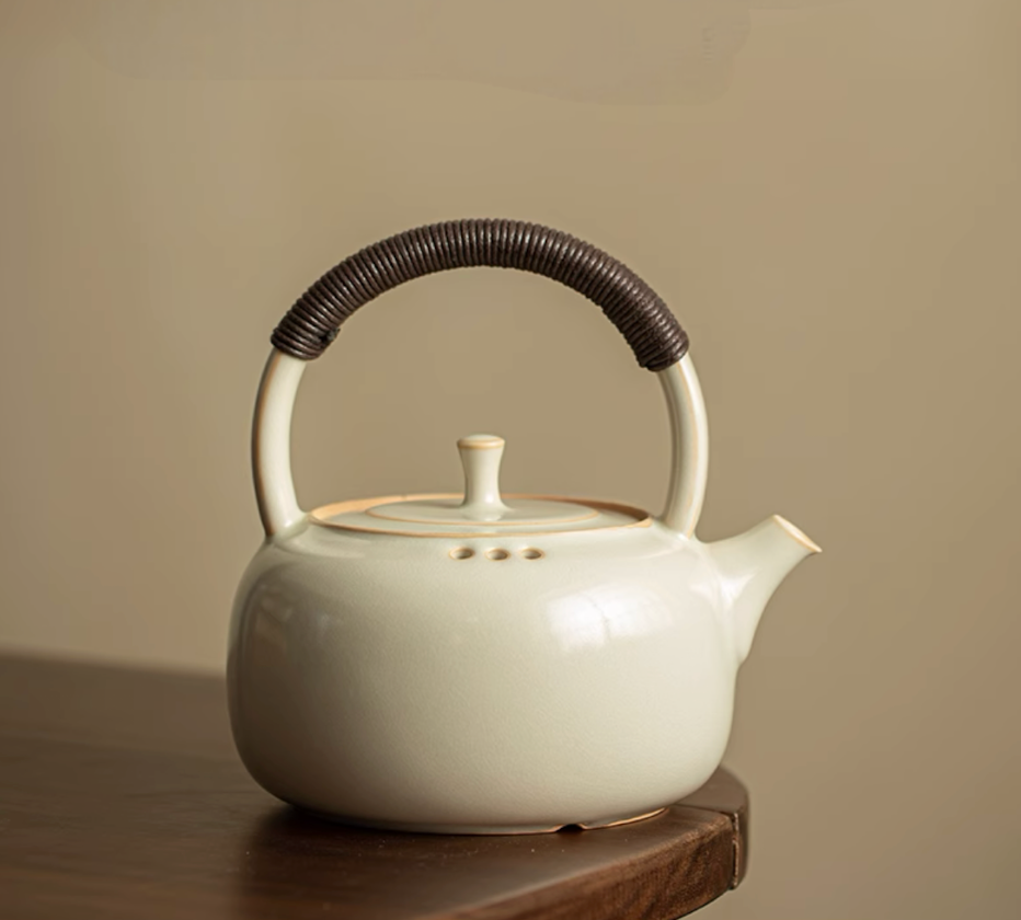 Soda Glaze Ceramic Teapot in off-white front view showing rounded body, lid, and wrapped handle placed on a wooden table