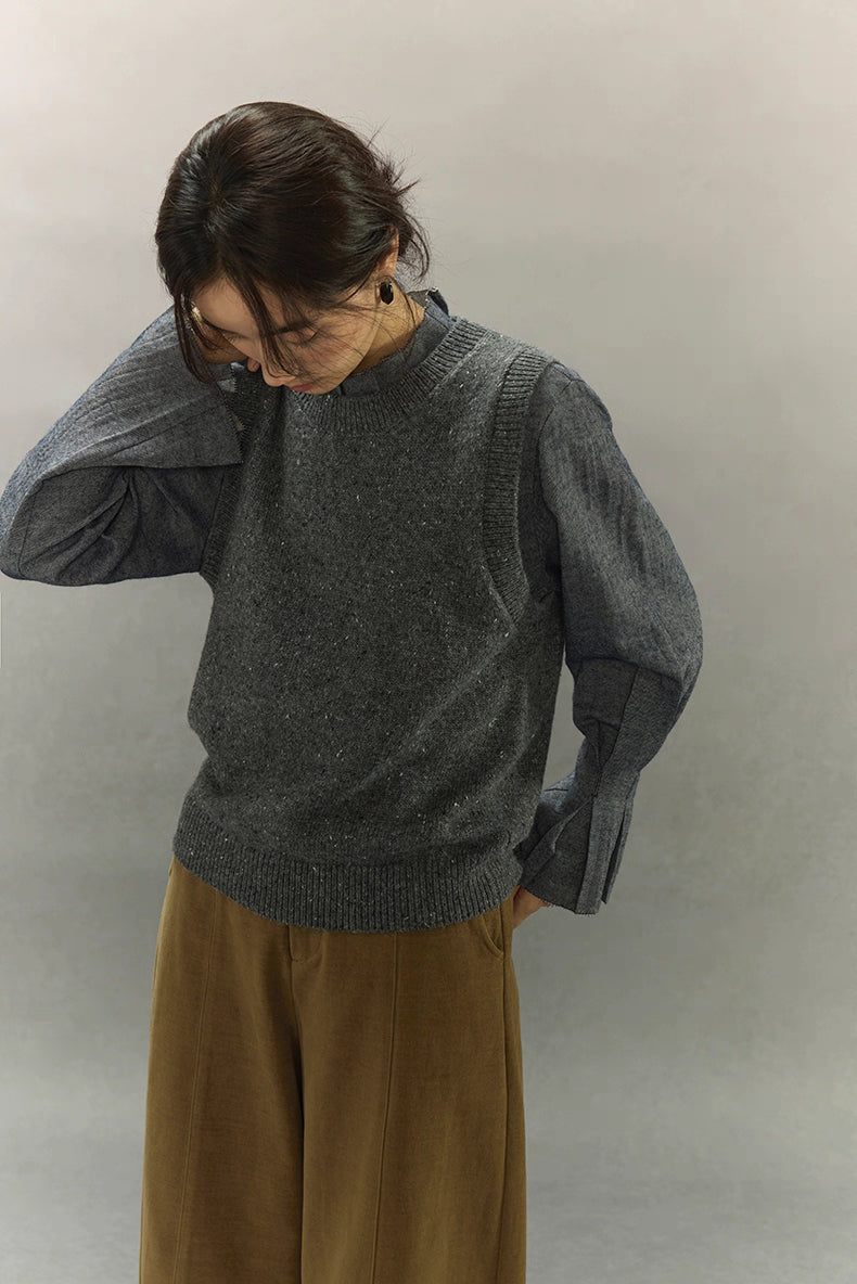 Woman looking down while wearing speckled knit vest layered over a blue shirt.