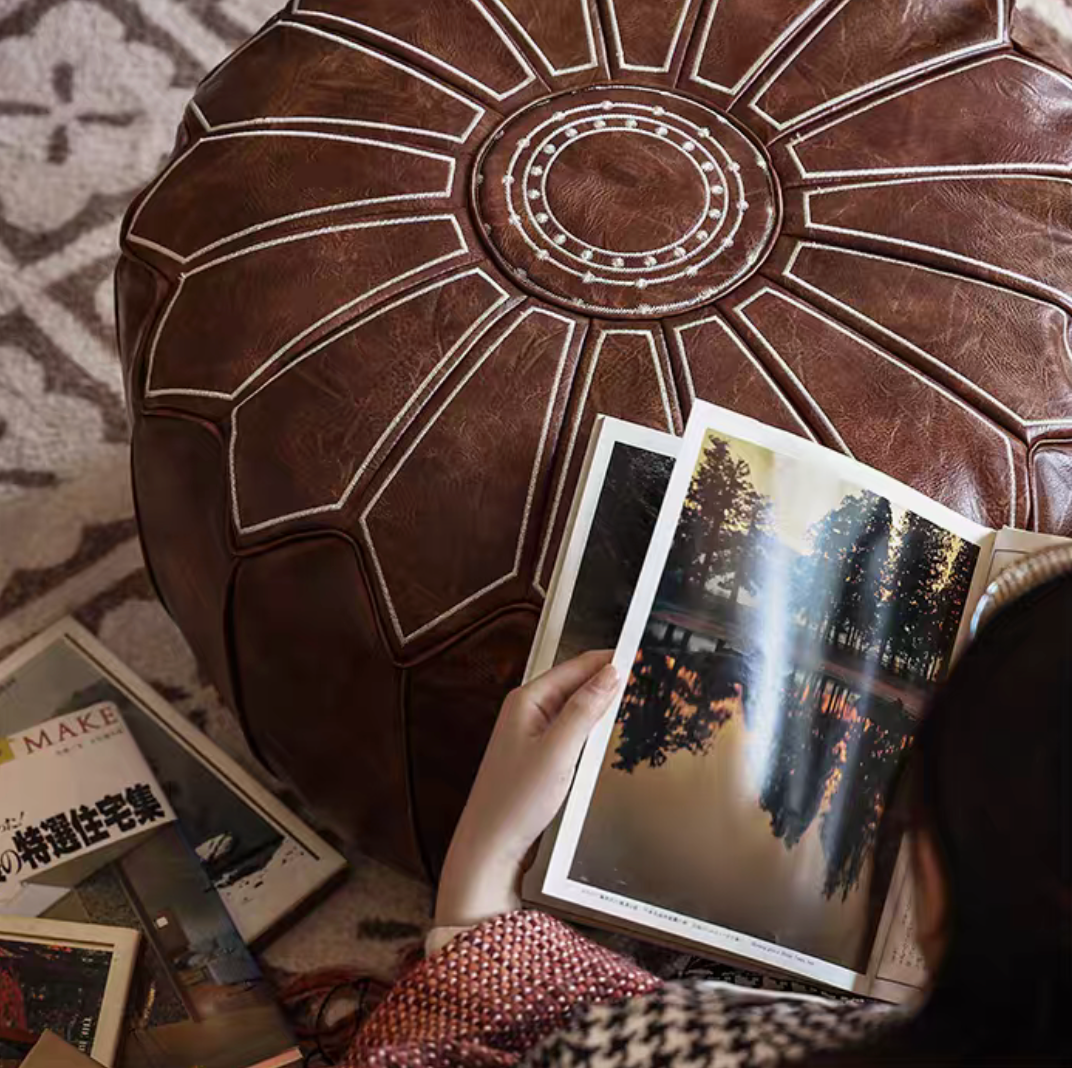 Top view of camel faux leather pouf ottoman with open book showing stitched sunburst embroidery