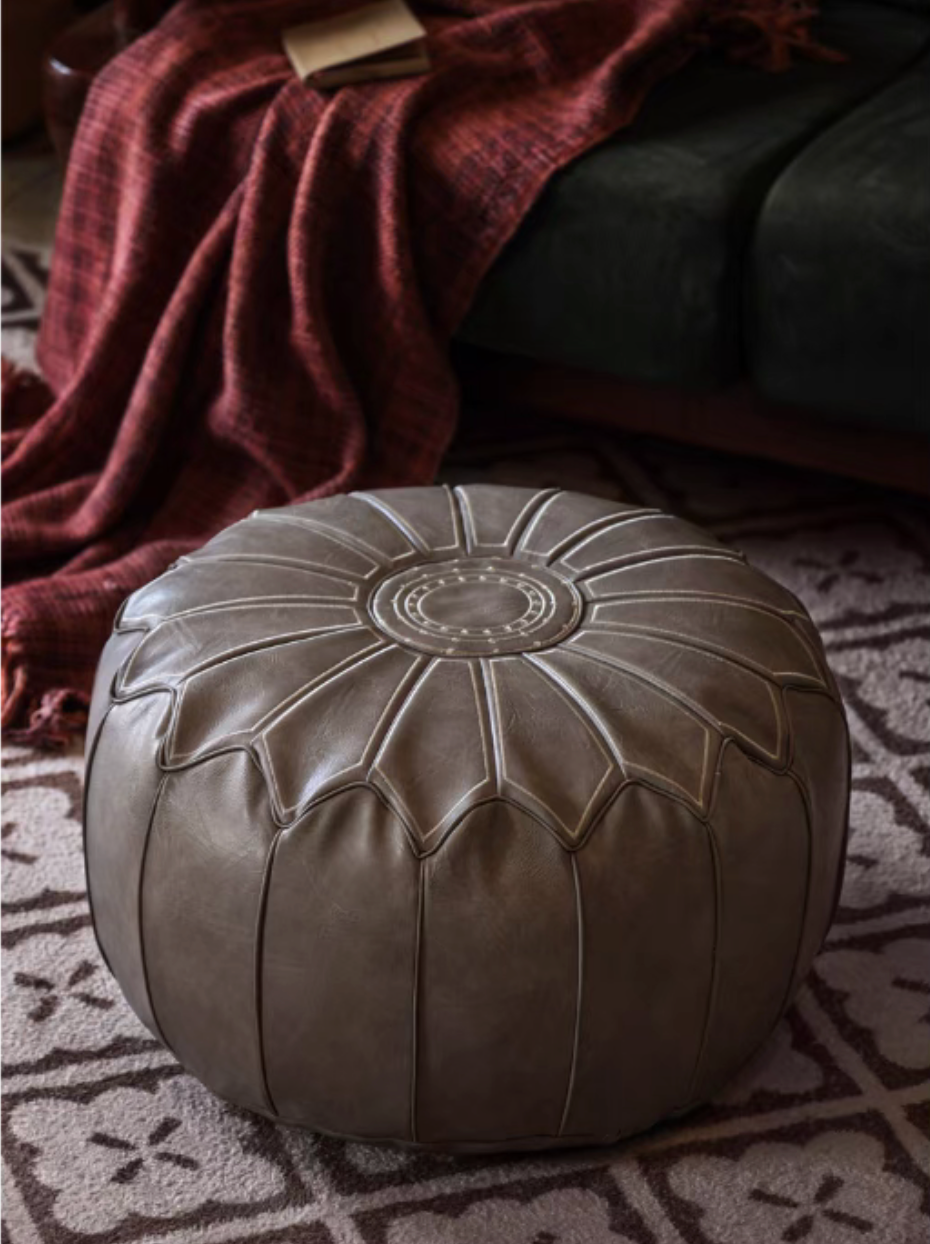 Gray faux leather pouf ottoman placed on patterned rug beside sofa in a cozy interior setting